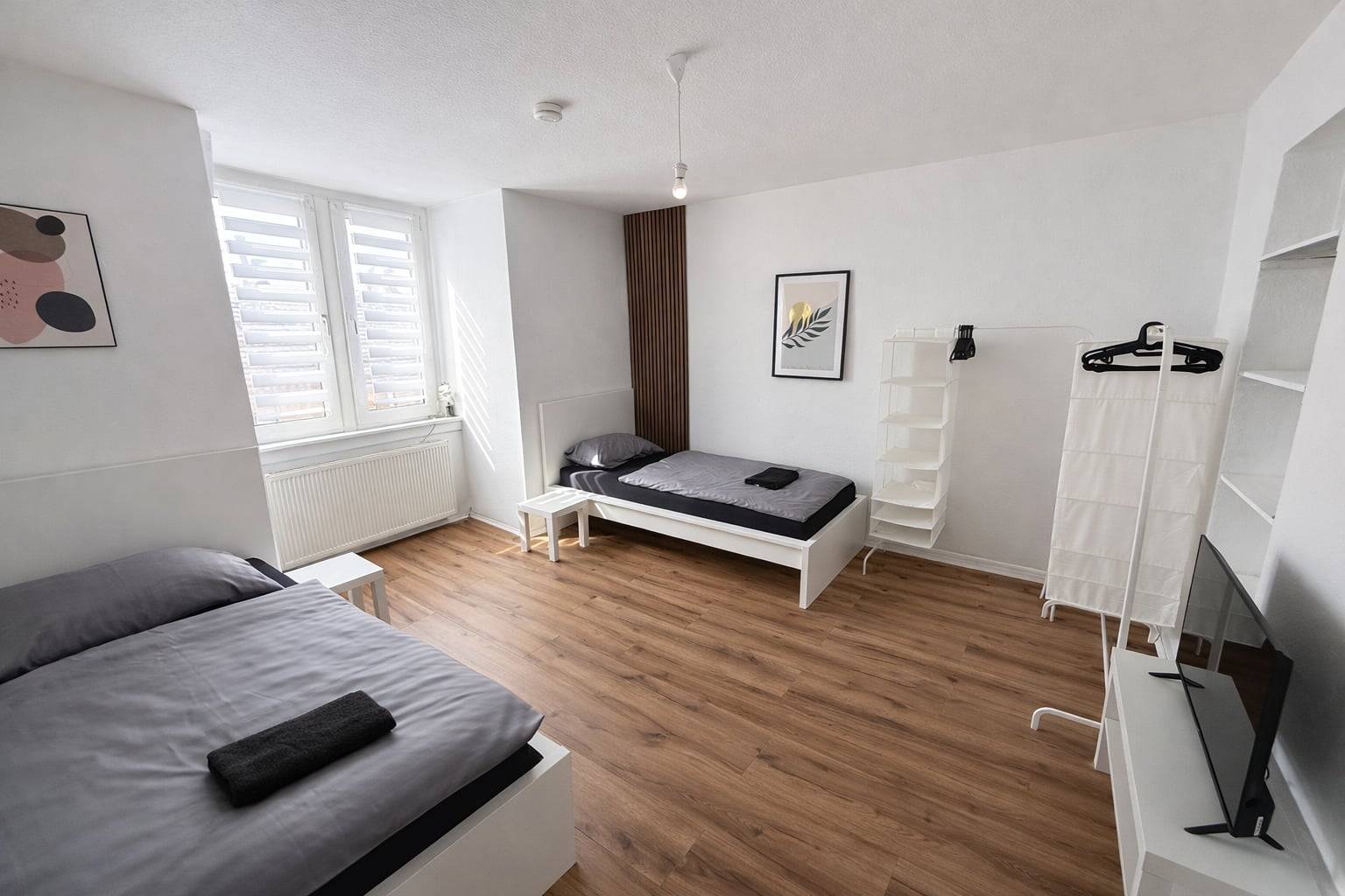 Zimmer mit zwei Einzelbetten, Regalen, Kleiderständer und Fernseher in der Monteurwohnung in Frankfurt am Main