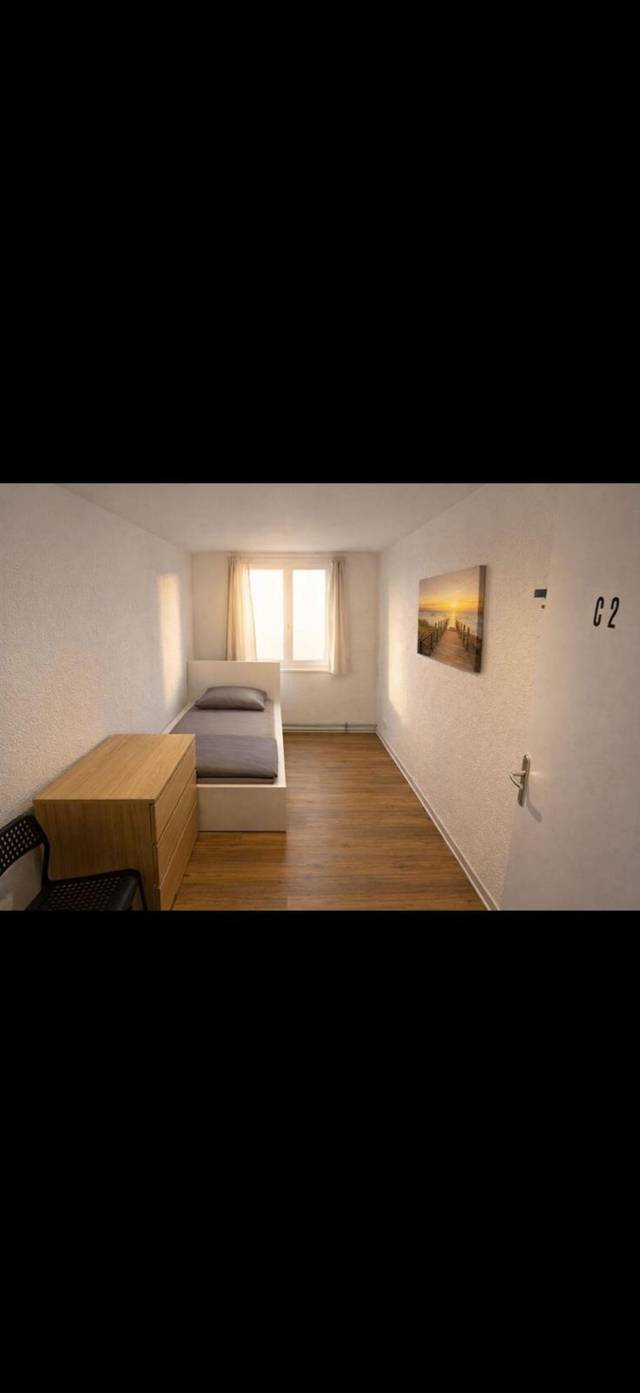 Schmales Zimmer mit Einzelbett, Kommode und Stuhl in einem Monteurzimmer in Frankfurt am Main