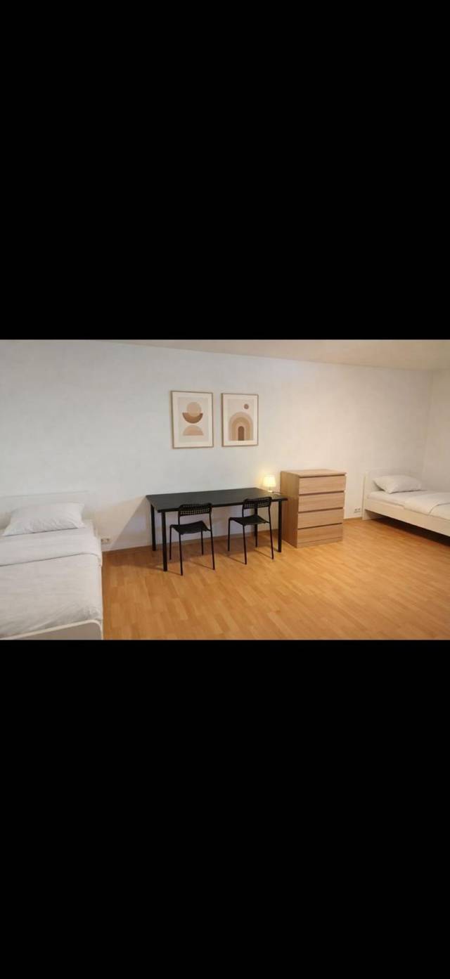 Tisch mit zwei Stühlen und Kommode zwischen Betten in einem Monteurzimmer in Frankfurt am Main