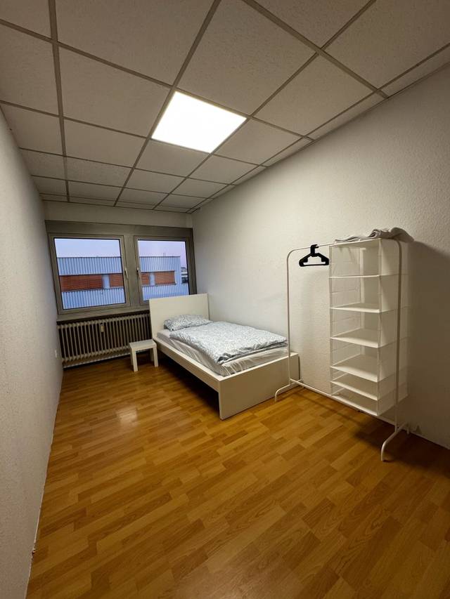 Zimmer mit Einzelbett, Kleiderständer und Heizkörper unter dem Fenster in der Monteurwohnung in Dreieich