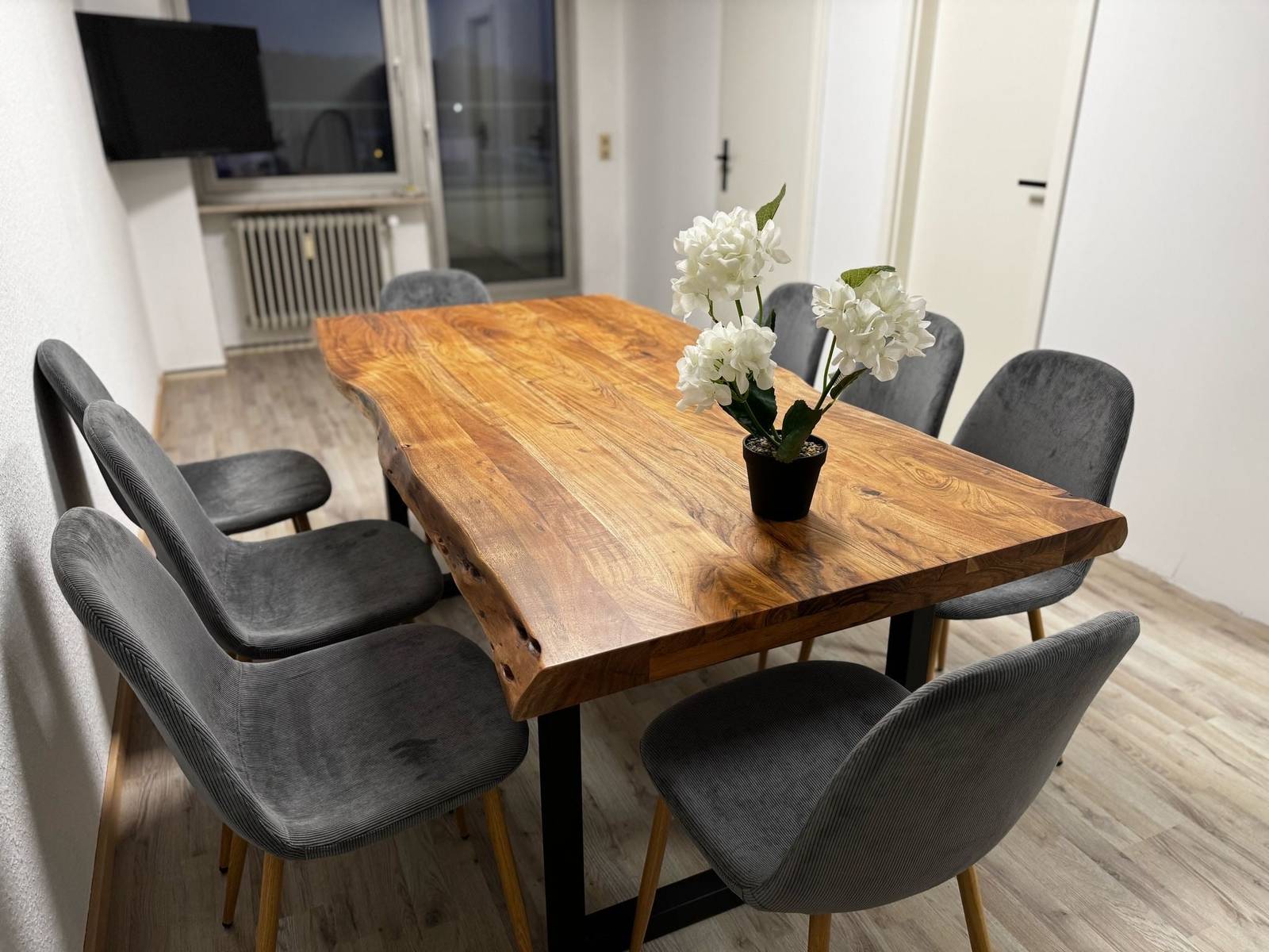 Holztisch mit grauen Polsterstühlen und Fernseher an der Wand in einer Monteurwohnung in Dreieich