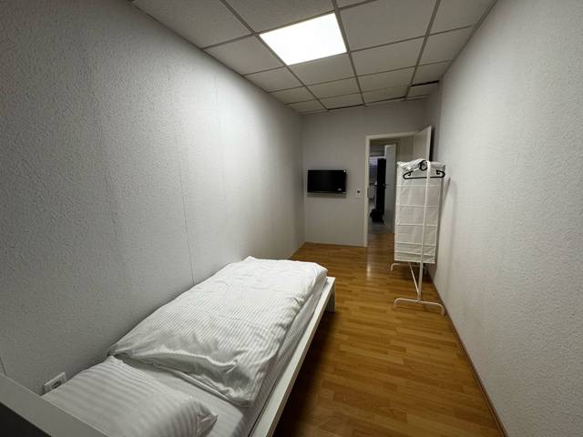 Zimmer mit Einzelbett, Kleiderständer und Wandfernseher in der Monteurwohnung in Dreieich