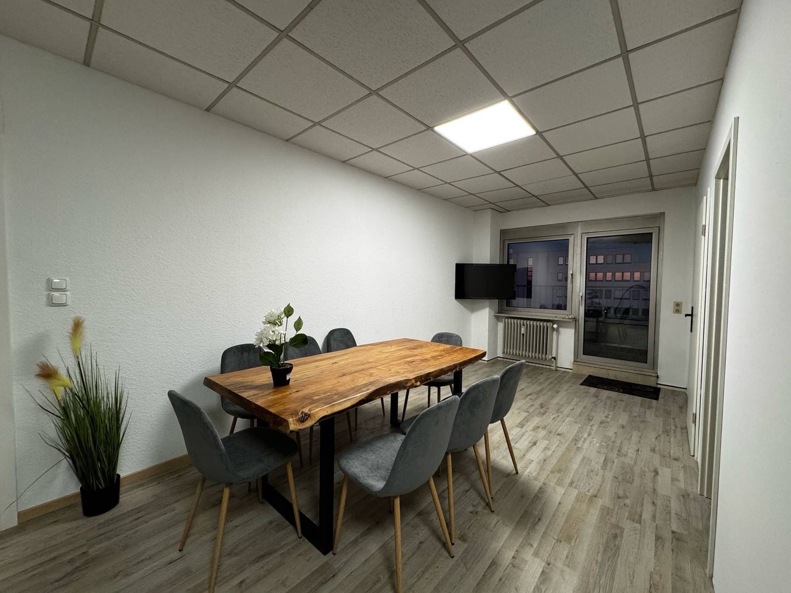 Essbereich mit Holztisch, grauen Stühlen, Fernseher und Balkontür in der Monteurwohnung in Dreieich