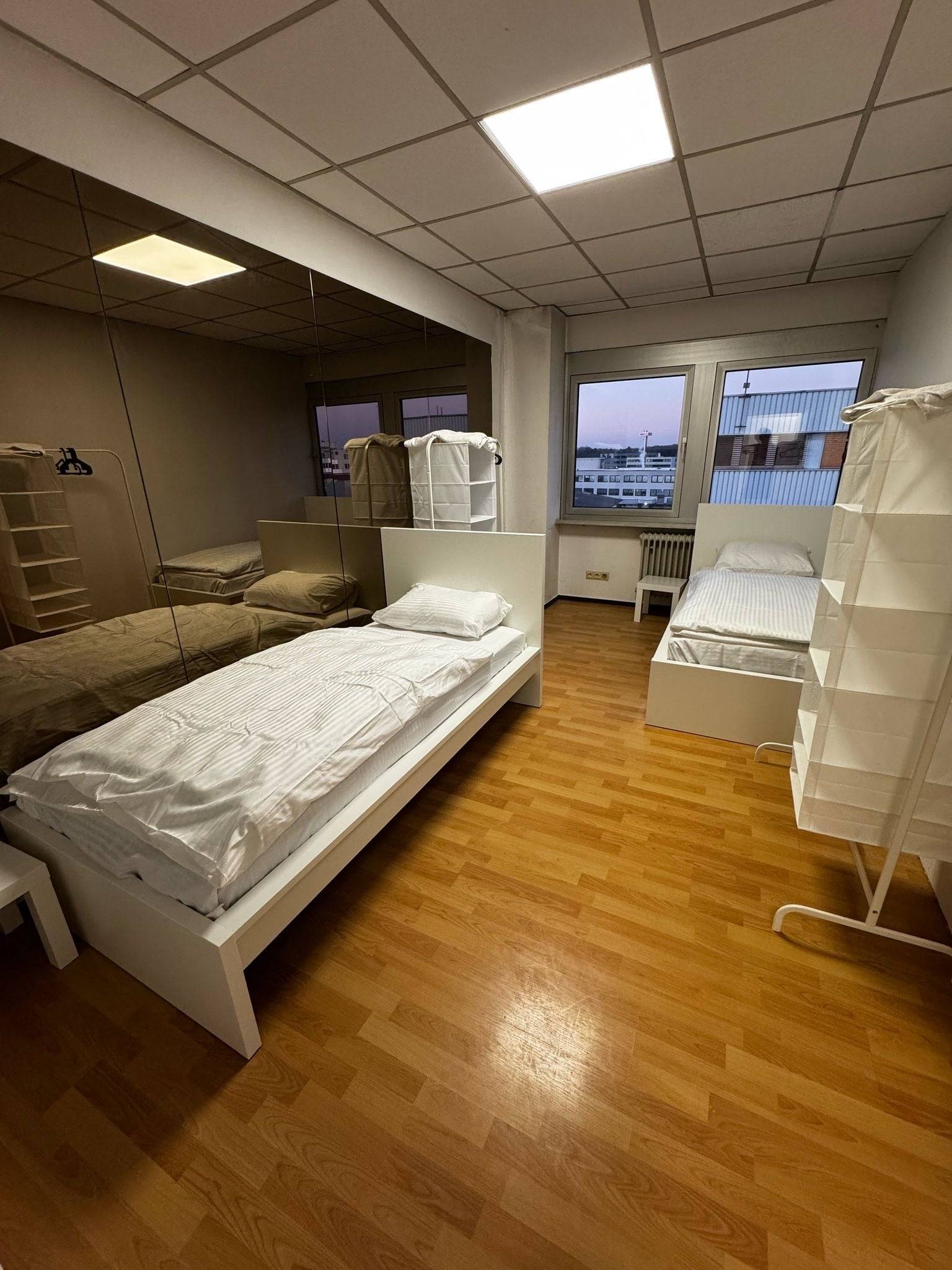 Zwei Einzelbetten mit weißer Bettwäsche und Wandspiegel in einem Zimmer der Monteurwohnung in Dreieich