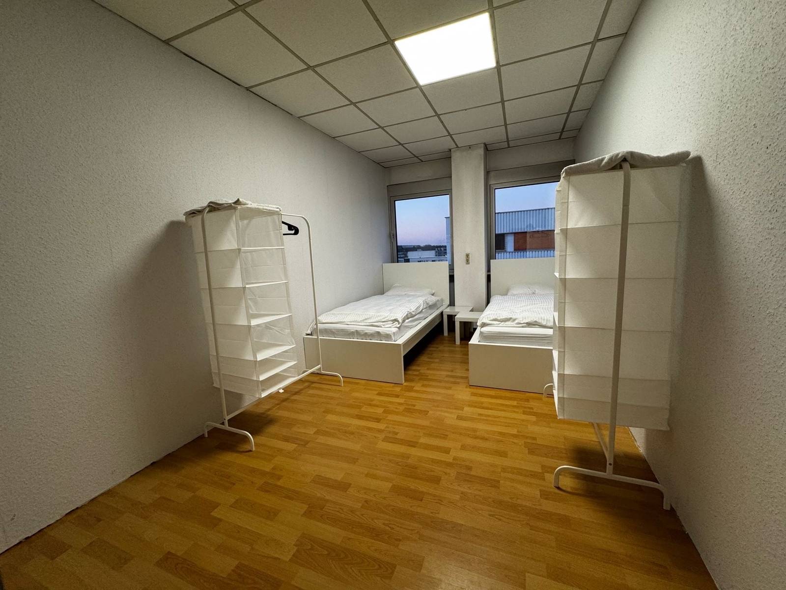 Zwei Einzelbetten und zwei Kleiderständer mit Stoffregalen in einem Zimmer der Monteurwohnung in Dreieich