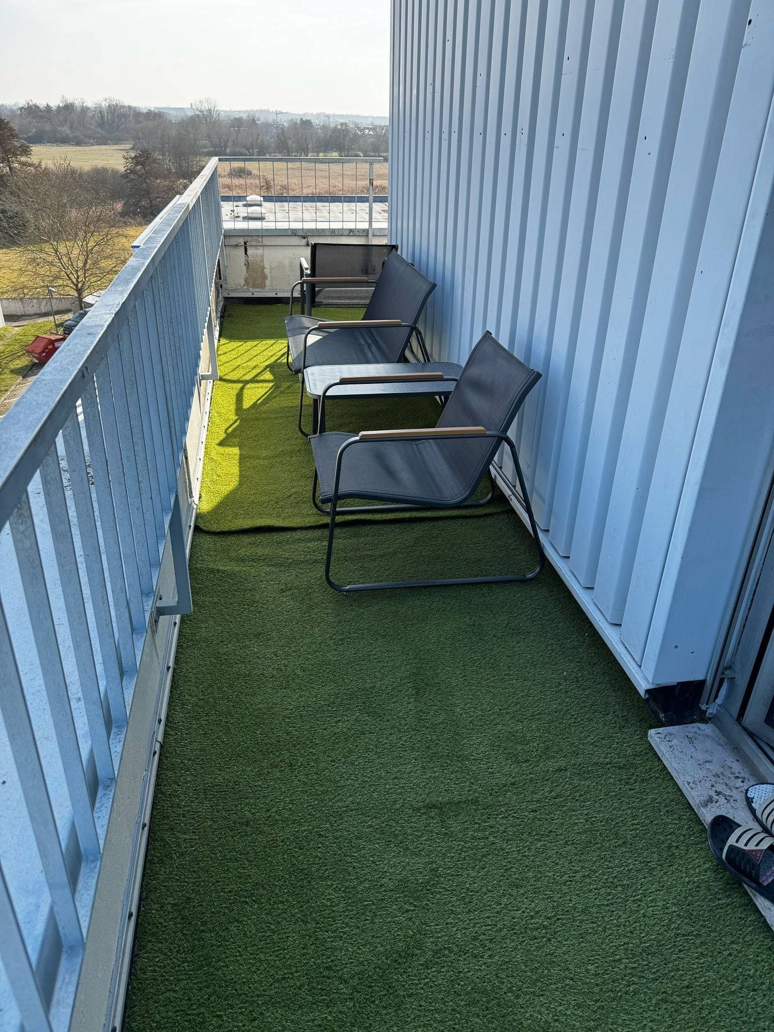 Zwei Stühle und ein Beistelltisch auf dem Balkon mit Kunstrasen einer Monteurwohnung in Dreieich