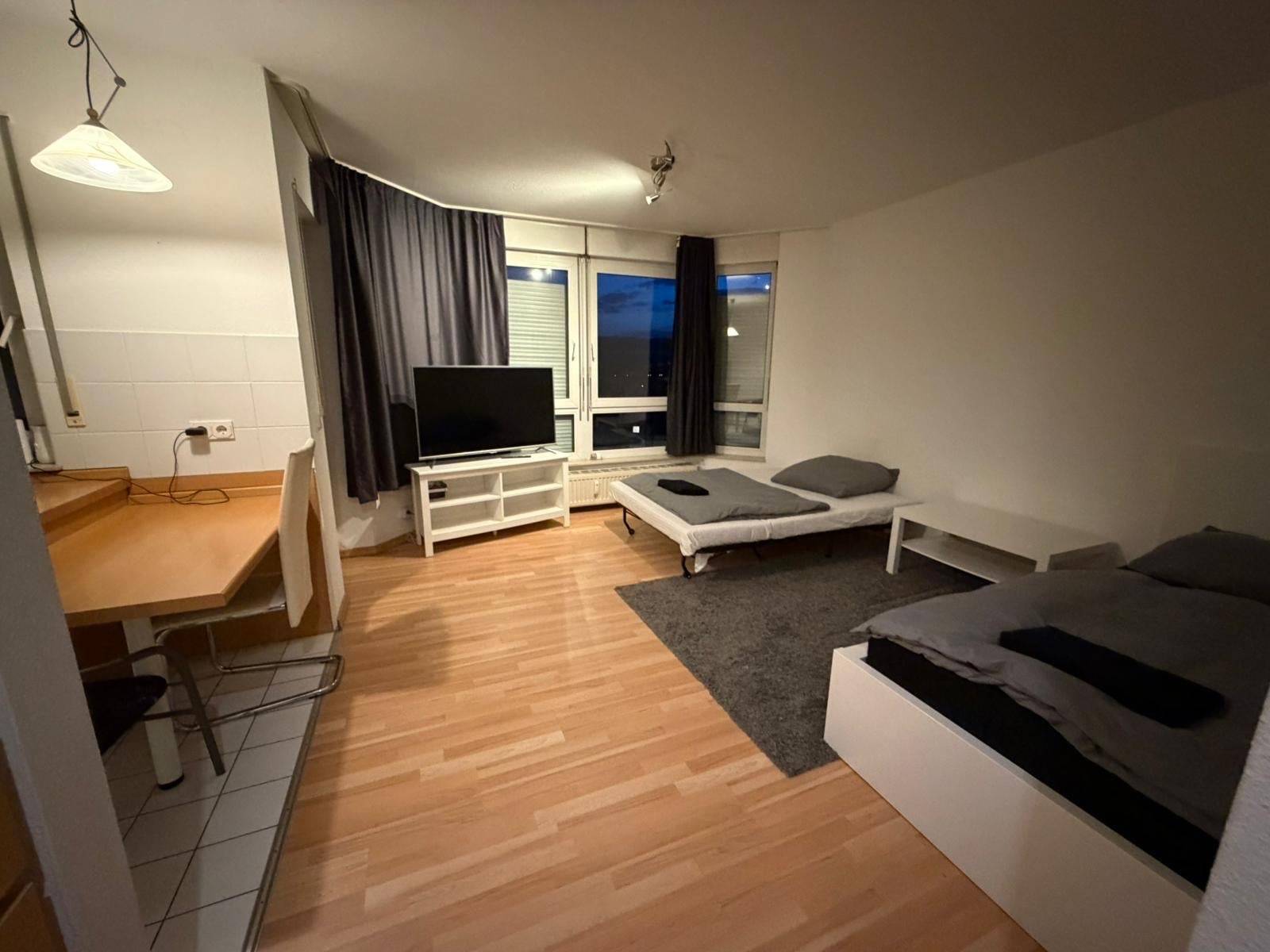 Wohnraum mit zwei Betten, Fernseher und Theke mit Stuhl in der Monteurwohnung in Niedernhausen