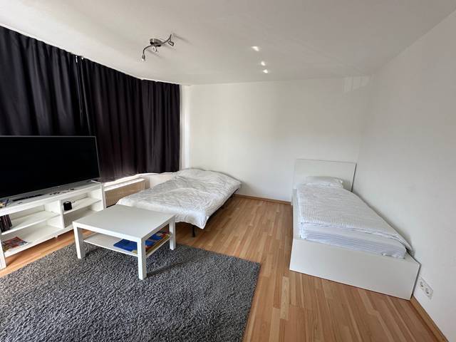 Einzelbett, Bettsofa, Couchtisch und Fernseher im Wohnraum einer Monteurwohnung in Niedernhausen