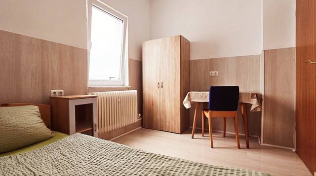 Schlafzimmer mit Bett, Kleiderschrank, Heizkörper und Tisch mit Stuhl in der Monteurwohnung in Frankfurt am Main