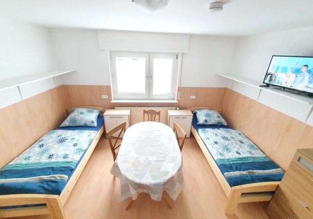 Zimmer mit zwei Einzelbetten, ovalem Tisch, Stühlen und Fernseher in der Monteurwohnung in Frankfurt am Main