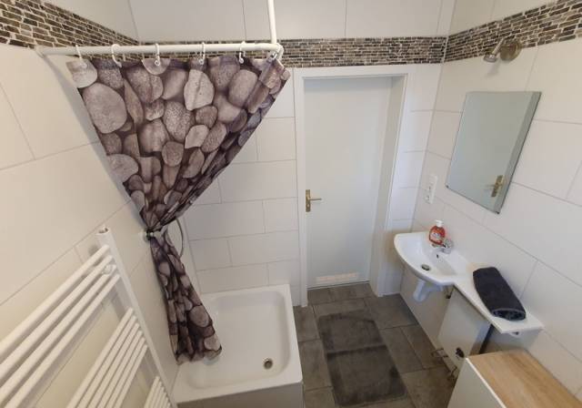 Badezimmer mit Duschwanne, Vorhang, Waschbecken und Spiegel in einer Monteurwohnung in Frankfurt am Main