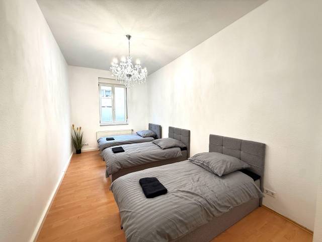 Drei Einzelbetten mit grauen Kopfteilen und Heizkörper unter dem Fenster einer Monteurwohnung in Frankfurt am Main