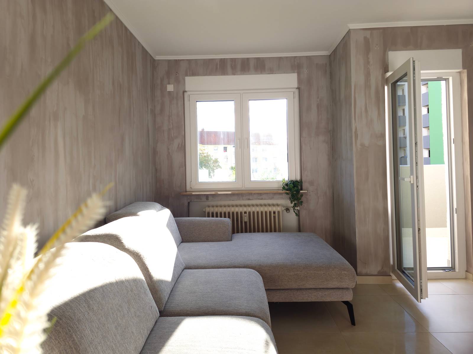 Ecksofa mit Heizkörper am Fenster und geöffneter Balkontür in der Monteurwohnung in Hanau