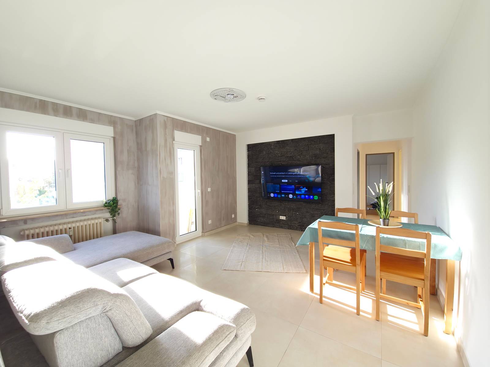 Wohnbereich mit Ecksofa, Wand-TV und Esstisch mit Stühlen in der Monteurwohnung in Hanau