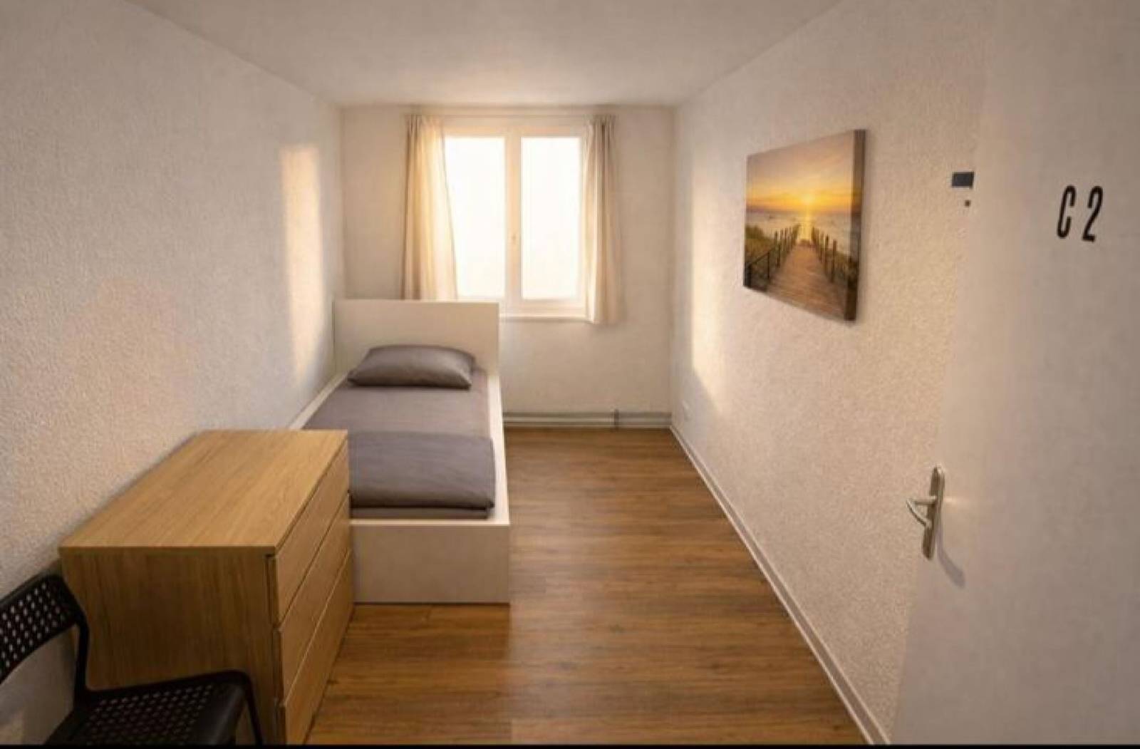 Einzelbett mit Kommode vor einem Fenster in einem Zimmer eines Monteurzimmers in Rüsselsheim
