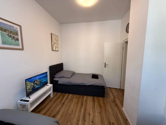 Einzelbett mit Polsterkopfteil und Fernseher neben der Tür in der Monteurwohnung in Frankfurt am Main