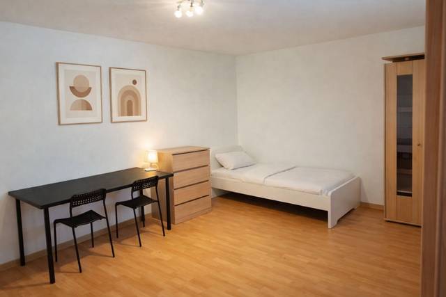 Einzelbett, langer Schreibtisch mit zwei Stühlen, Kommode und Schrank in einem Monteurzimmer in Frankfurt am Main