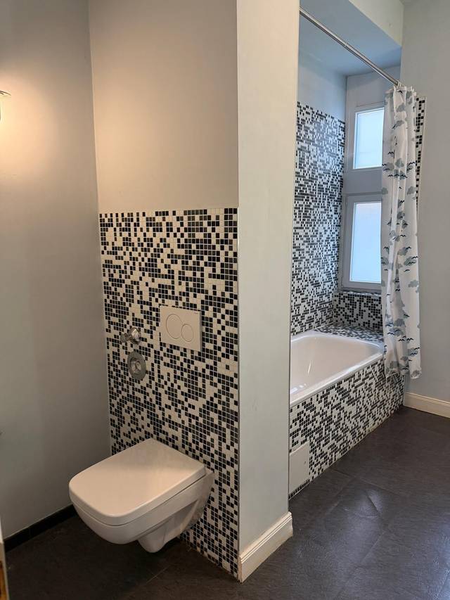 Badewanne mit Duschvorhang und Wand-WC vor Mosaikfliesen in der Monteurwohnung in Frankfurt am Main