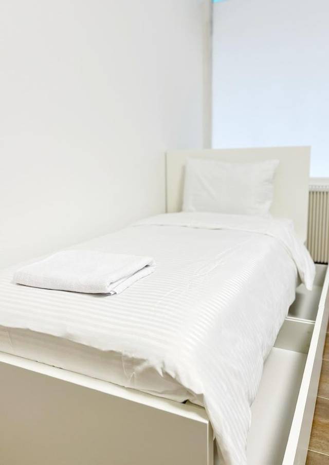 Einzelbett mit gestreifter Bettwäsche und gefaltetem Handtuch in einer Monteurwohnung in Wiesbaden