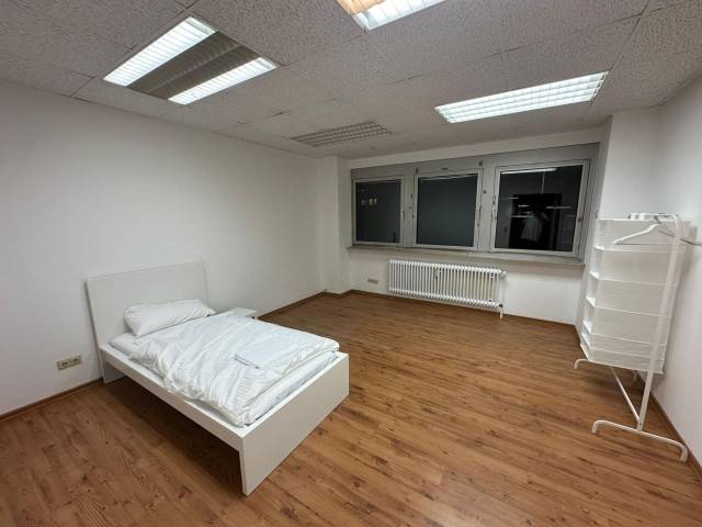 Zimmer mit Einzelbett, Kleiderständer und Heizkörper unter dem Fenster in einer Monteurwohnung in Frankfurt am Main