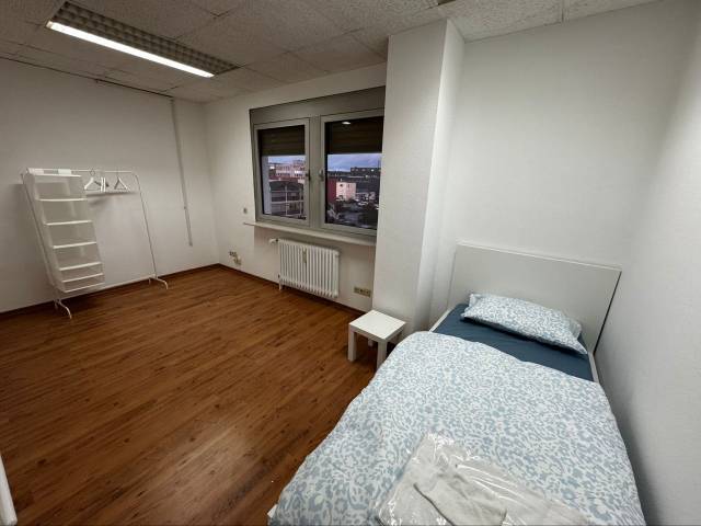 Einzelbett mit hellblauer Bettwäsche und Kleiderständer in einem Zimmer der Monteurwohnung in Frankfurt am Main