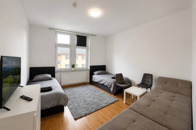 Zimmer mit zwei Einzelbetten, Sofa, Fernseher und zwei Stühlen in einer Monteurwohnung in Frankfurt am Main