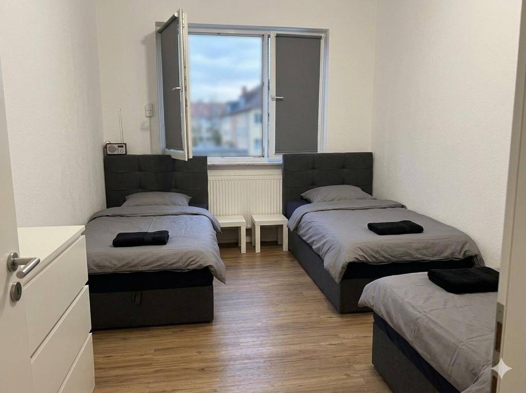 Drei Einzelbetten mit grauer Bettwäsche und Kommode in der Monteurwohnung in Mainz