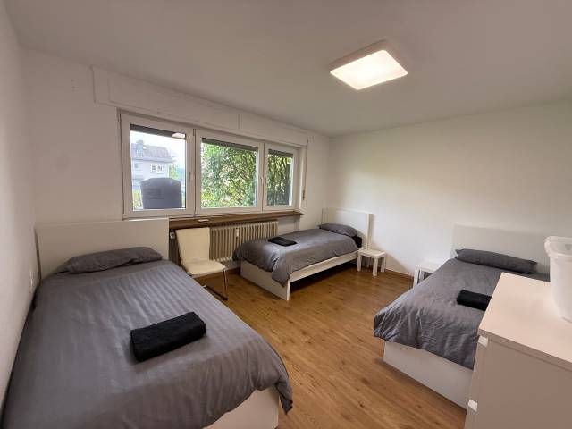 Schlafzimmer mit drei Einzelbetten, Stuhl und Kommode in einer Monteurwohnung in Niedernhausen
