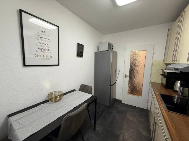 Schmaler Esstisch mit Stühlen und Kühlschrank in der Küche einer Monteurwohnung in Niedernhausen
