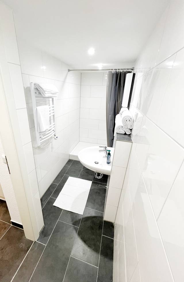 Schmales Bad mit Duschvorhang, Waschbecken und Handtüchern in der Monteurwohnung in Walluf